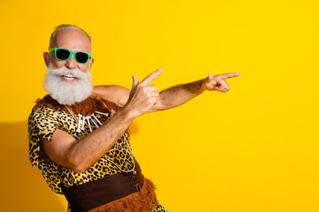 Portrait of primeval caveman dance point fingers empty space wear leopard skin clothes isolated on yellow color backgroundの写真素材