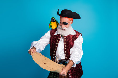 Photo portrait of old funny pirate male look hold treasure map dressed carnival party costume party isolated blue color backgroundの写真素材