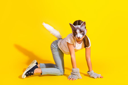 Young girl wearing a cat mask and tail posing against a vibrant yellow background with playful energy and creative disguiseの写真素材