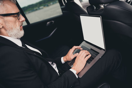 Mature businessman in formalwear working on laptop inside car on city streetの写真素材