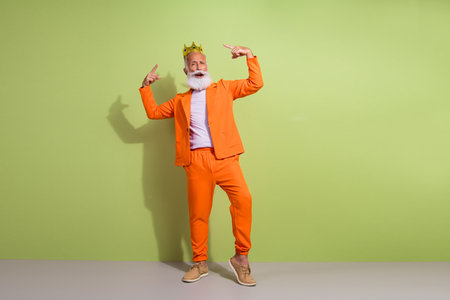 Full size portrait of aged man performer point fingers golden crown wear orange suit isolated on green color backgroundの写真素材