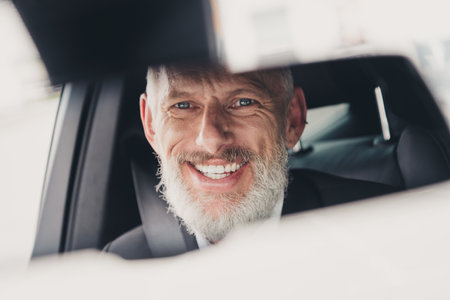 Confident senior businessman smiling in rearview mirror while sitting in car on city street