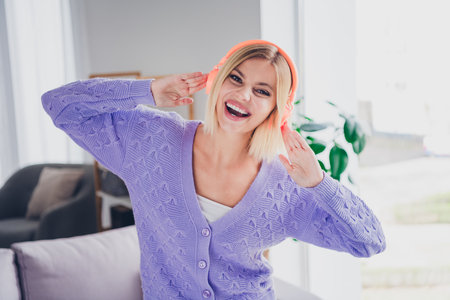 Charming young woman enjoying music at home in cozy cardiganの写真素材