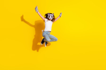 Energetic young girl in a cat mask jumping against a vibrant yellow backgroundの写真素材