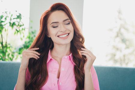 Photo of nice young ginger girl touch hair enjoy shampoo sit couch wear pink clothes enjoy modern cozy interior flat indoorsの写真素材