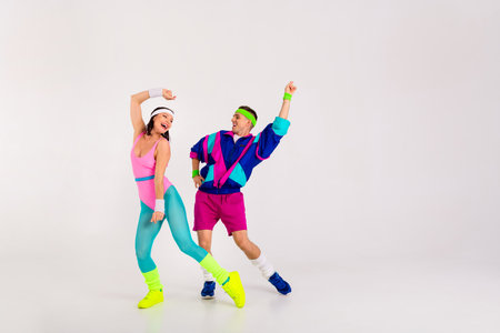 Energetic couple in vibrant retro activewear dancing with enthusiasm on a white background