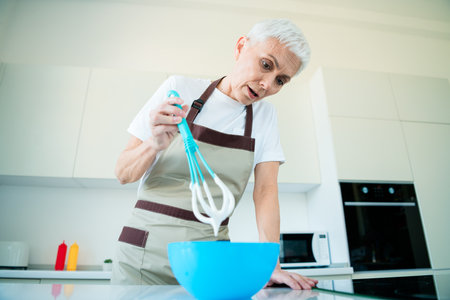 Senior woman in kitchen whisking ingredients in bowl, preparing a delicious homemade dish with focused attention and joyの写真素材