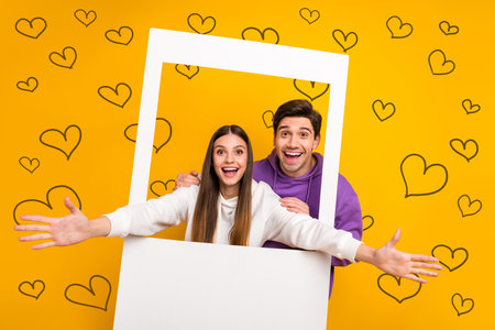 Portrait of two crazy carefree people make instant frame photo raise opened arms isolated on yellow color backgroundの写真素材