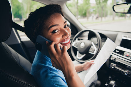 Young woman chatting on phone while driving car on a sunny dayの写真素材