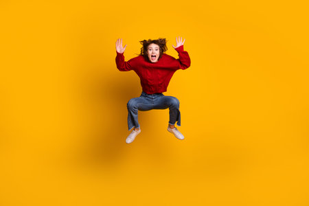 Excited woman jumping against a vibrant yellow backdrop, dressed in casual stylish attire