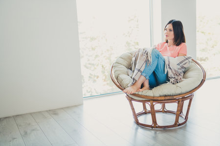Young woman relaxing at home in a stylish wicker chair with large window and daylightの写真素材