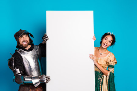 Medieval couple in themed costumes posing with blank board over vibrant pink backdropの写真素材