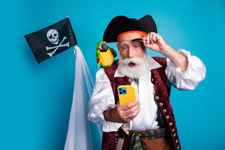 Photo portrait of bearded pirate man amazed hold gadget wear hallooween costume isolated on blue color background