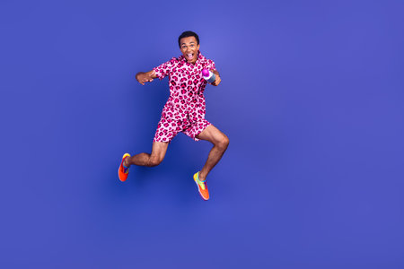 Young man in pink leopard print outfit jumping against a purple background, combining stylish fashion and joyful energyの写真素材
