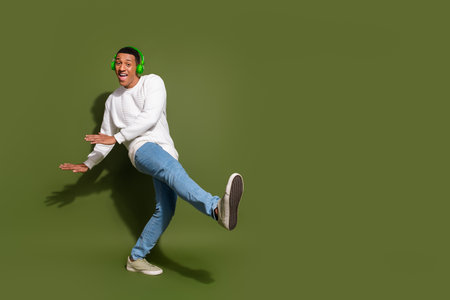 Energetic young man enjoying music with vibrant headphones, dancing happily against a khaki...