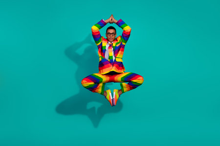 Charismatic young man in vibrant rainbow suit posing dynamically against teal background