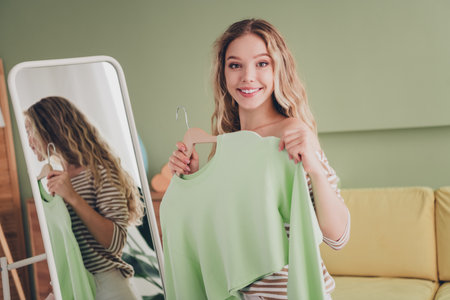 Happy young woman in a striped pullover enjoying a weekend at home, trying on clothes, smiling in her comfortable living room, and embracing a relaxed lifestyle with daylight pouring in.の写真素材