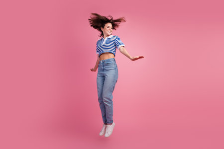 Young woman jumping with joy against a vibrant pink background, showcasing a playful mood and...
