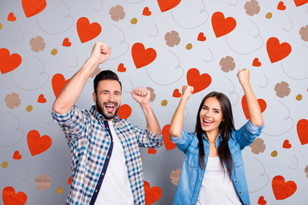 Portrait of young caucasian partners celebrating victory with raised fists over grey backgroundの写真素材