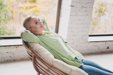 Young woman relaxing in a comfortable chair near a sunny window in a cozy living roomの写真素材