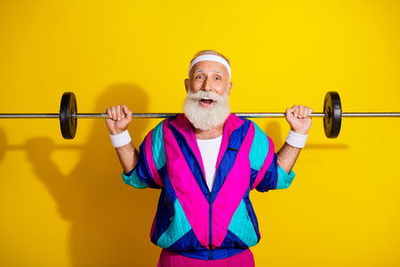 Photo portrait banner of funny senior sportsman hold shoulders barbell dressed retro sport costume isolated on yellow color backgroundの写真素材