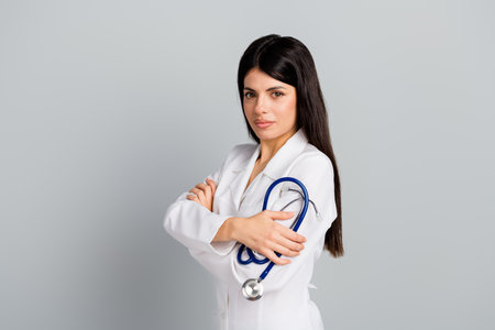 Female doctor in white coat holding stethoscope on grey background, representing medical professionalism and healthcare expertiseの写真素材