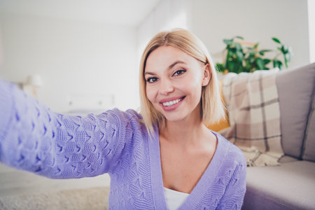 Smiling young woman with blond hair in cozy living room enjoying relaxing weekend indoorsの写真素材