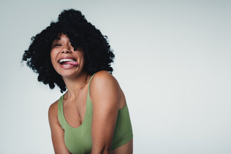 Joyful young woman showing confidence with big smile in green activewear against a grey backgroundの写真素材