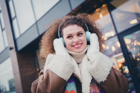 Portrait of nice young girl toothy smile touch headphones wear jacket walk snowy weather city street outdoorsの写真素材