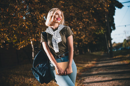 Photo of pretty young blonde woman walk college hold book wondered wear khaki clothes tied shoulders...