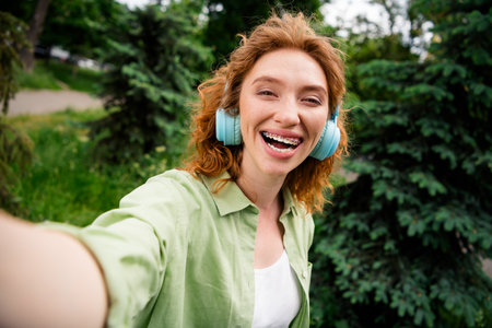 Young redhaired woman enjoying a sunny day outdoors with headphonesの写真素材