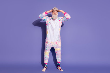 Trendy man in unicorn pajama poses against a vibrant purple background.の写真素材