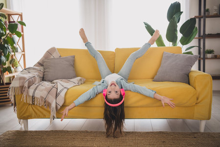 Young girl with headphones enjoying her weekend upside down on a cozy yellow sofa in living roomの写真素材