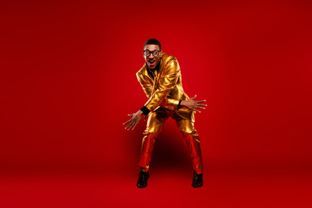 Charismatic young man in a stylish golden suit striking a playful pose against a vivid red background, exuding charm and funの写真素材