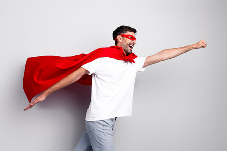 Young man in red superhero attire striking a dynamic pose against a neutral backgroundの写真素材