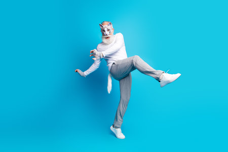 Elderly man with cat mask posing dynamically in stylish casual wear on vibrant blue backgroundの写真素材