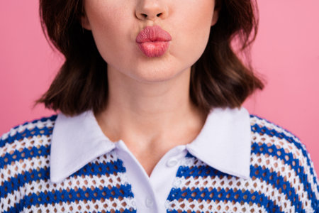 Stylish young woman making a playful kissy face against a pink background wearing a trendy knit top