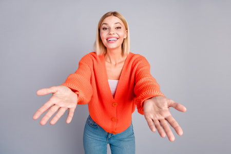 Portrait of nice young girl arms welcome you cuddle orange cardigan isolated on grey color backgroundの写真素材