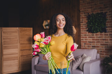 Cheerful young woman with afro hair arranging vibrant tulips in cozy living roomの写真素材