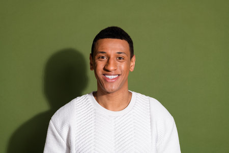 Confident young man smiling against khaki background wearing stylish white sweater