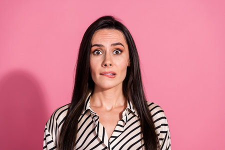 Surprised young woman with brunette hair against pink background wearing striped shirtの写真素材