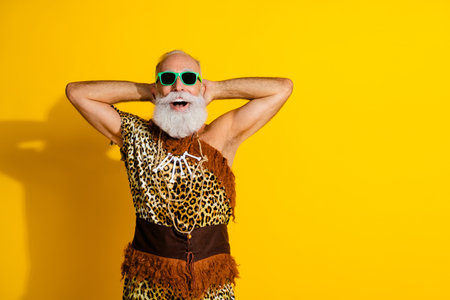 Photo of aged caveman hands behind head empty space wear leopard skin clothes isolated on yellow color backgroundの写真素材