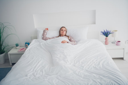 Young woman enjoying a peaceful nap in cozy bedroom, dressed in comfortable pajama, embracing the calmness of morning lightの写真素材