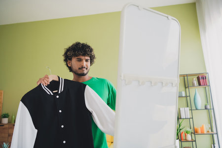 Photo of nice young man hold jacket look mirror wear t-shirt weekend green interior apartment indoorsの写真素材
