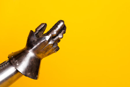 Metal knights armored hands in prayer gesture against bright yellow backgroundの写真素材