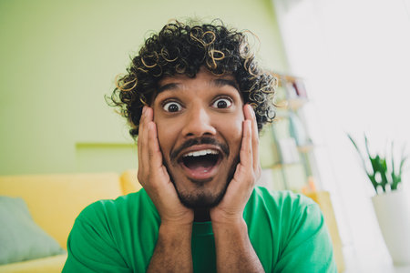 Photo of nice young man hands touch cheeks open mouth wear t-shirt modern green interior apartment...