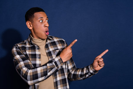 Photo portrait of handsome young man look point amazed empty space dressed stylish plaid garment isolated on dark blue color backgroundの写真素材