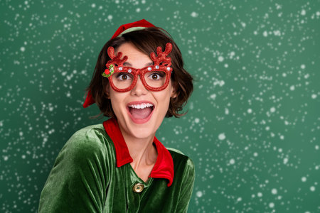Photo of impressed pretty young woman dressed elf costume deer glasses smiling empty space isolated green color backgroundの写真素材