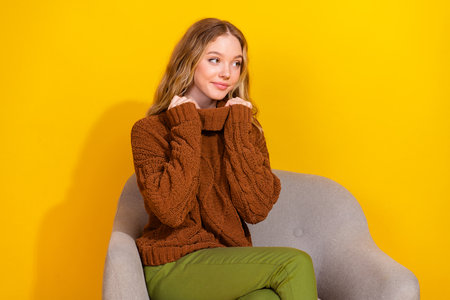 Photo of pretty young woman sit chair look empty space wear pullover isolated on yellow color backgroundの写真素材