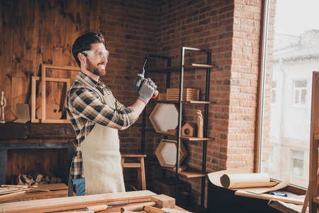 Photo of builder wood worker guy look in window use electronic drill in garage indoorsの写真素材